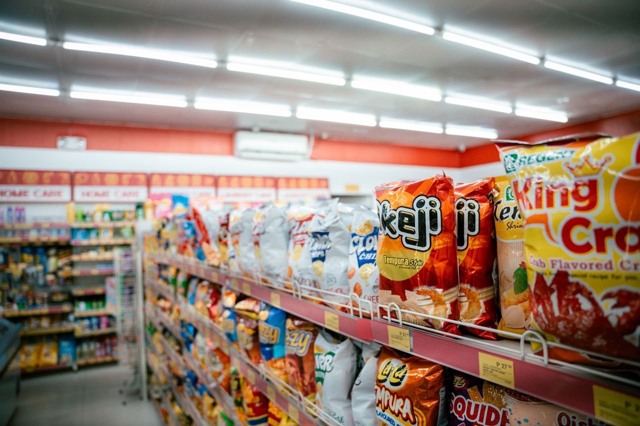 Free Wide shot of vibrant snack aisle in a supermarket with various chip bags on display. Stock Photo