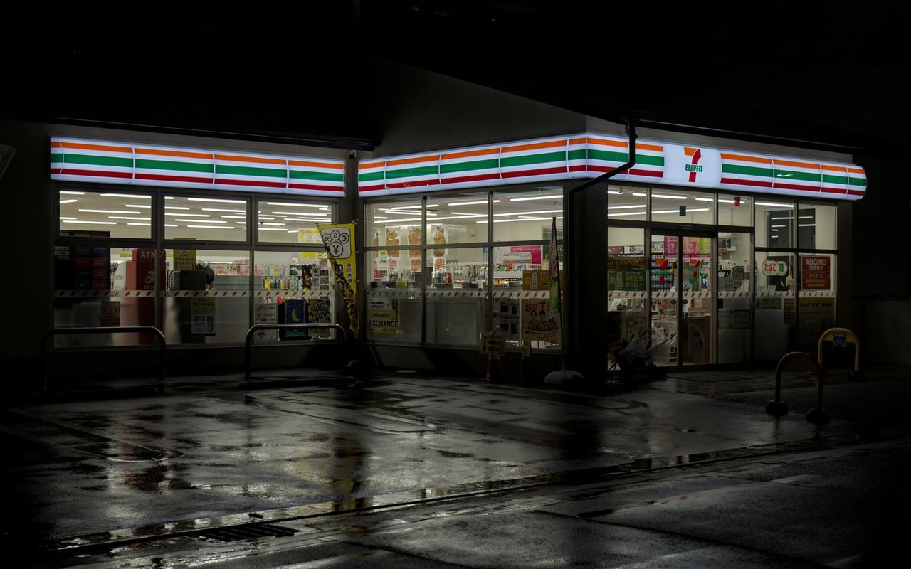 Free Illuminated 7-Eleven in Kyoto reflecting on wet street at night. Stock Photo