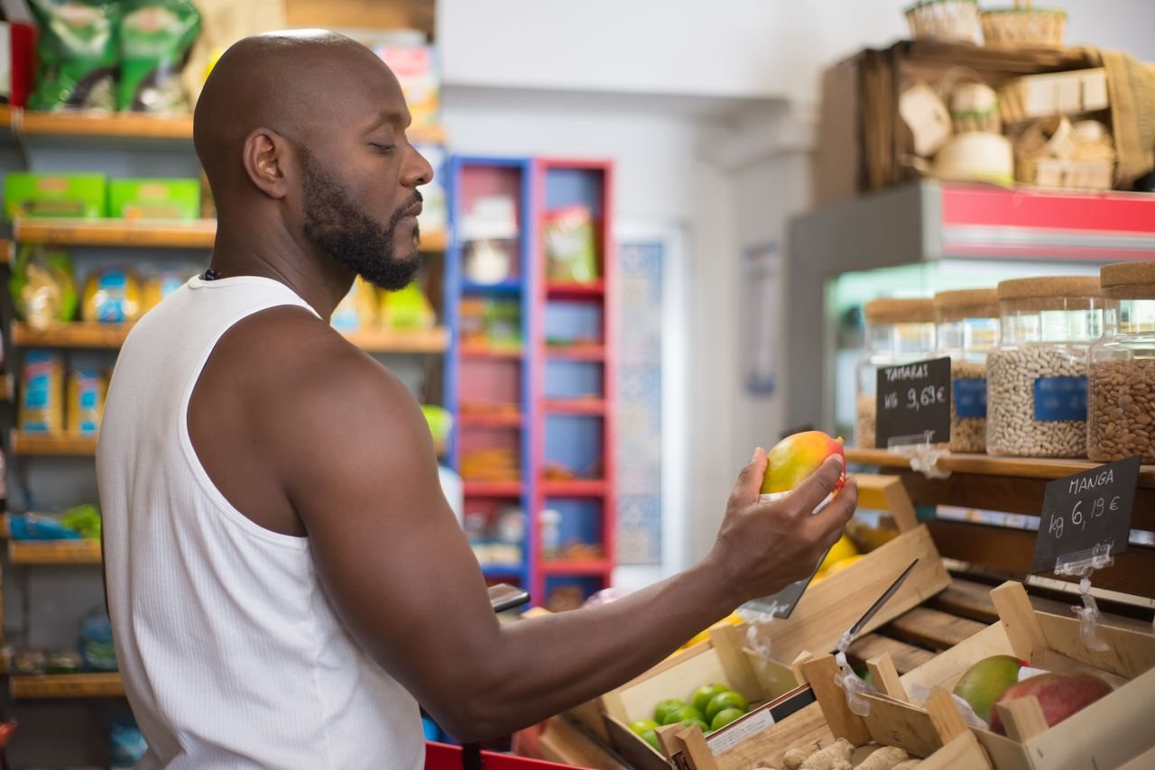 Free Adult man shopping for mangoes in a Portuguese supermarket, examining fruit quality. Stock Photo