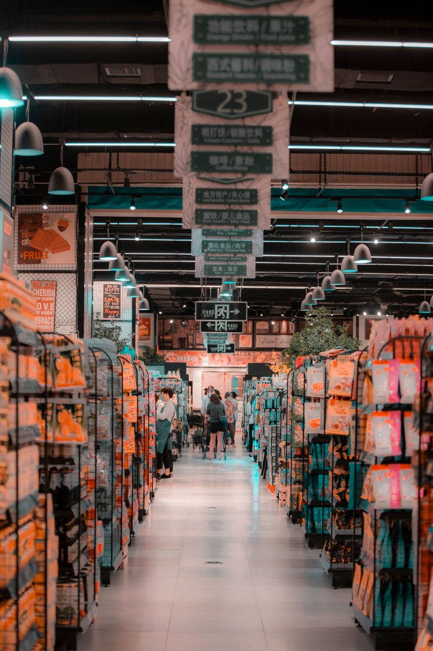 Free A bustling scene inside a supermarket aisle with shoppers and filled shelves under bright lighting. Stock Photo